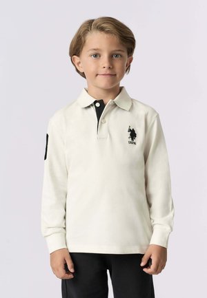 Polo a maniche lunghe colore crema con colletto nero, dotato di logo sul lato sinistro del petto e di una toppa sul lato sinistro della manica. Texture morbida.