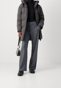 Doudoune grise foncée avec capuche, assortie à un pantalon large gris clair, des chaussures noires chunky et un petit sac à main noir.