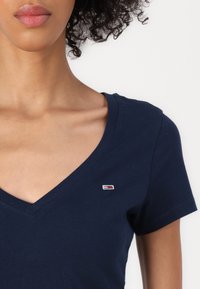 Marineblå V-hals t-skjorte laget av lett bomull. Har et lite brodert logo i rødt, hvitt og blått på brystet. Glatt tekstur.
