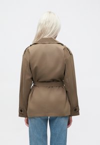 Braune Jacke mit Gürtel, klassischem Kragen, geknöpften Manschetten und glattem Stoff. Die Rückansicht zeigt eine taillierte Passform und strukturierte Schultern.