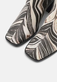 Botas até ao tornozelo em preto e branco com um padrão marmoreado, bico quadrado, textura suave e um salto baixo em bloco. Detalhes de costura visíveis.