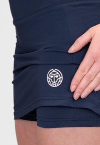 Shorts deportivos de color azul marino, confeccionados en un material elástico, con un acento de logo blanco en el lado izquierdo. Textura suave y diseño ajustado.