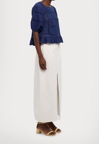 Blusa blu navy con trama, maniche a sbuffo e orlo arricciato; gonna lunga crema con spacco frontale; sandali giallo chiaro con tacco a blocco.