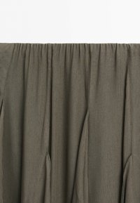 Close-up van donkerolijfgroene stof met verticale naden en een geplooide taillebanddetail.