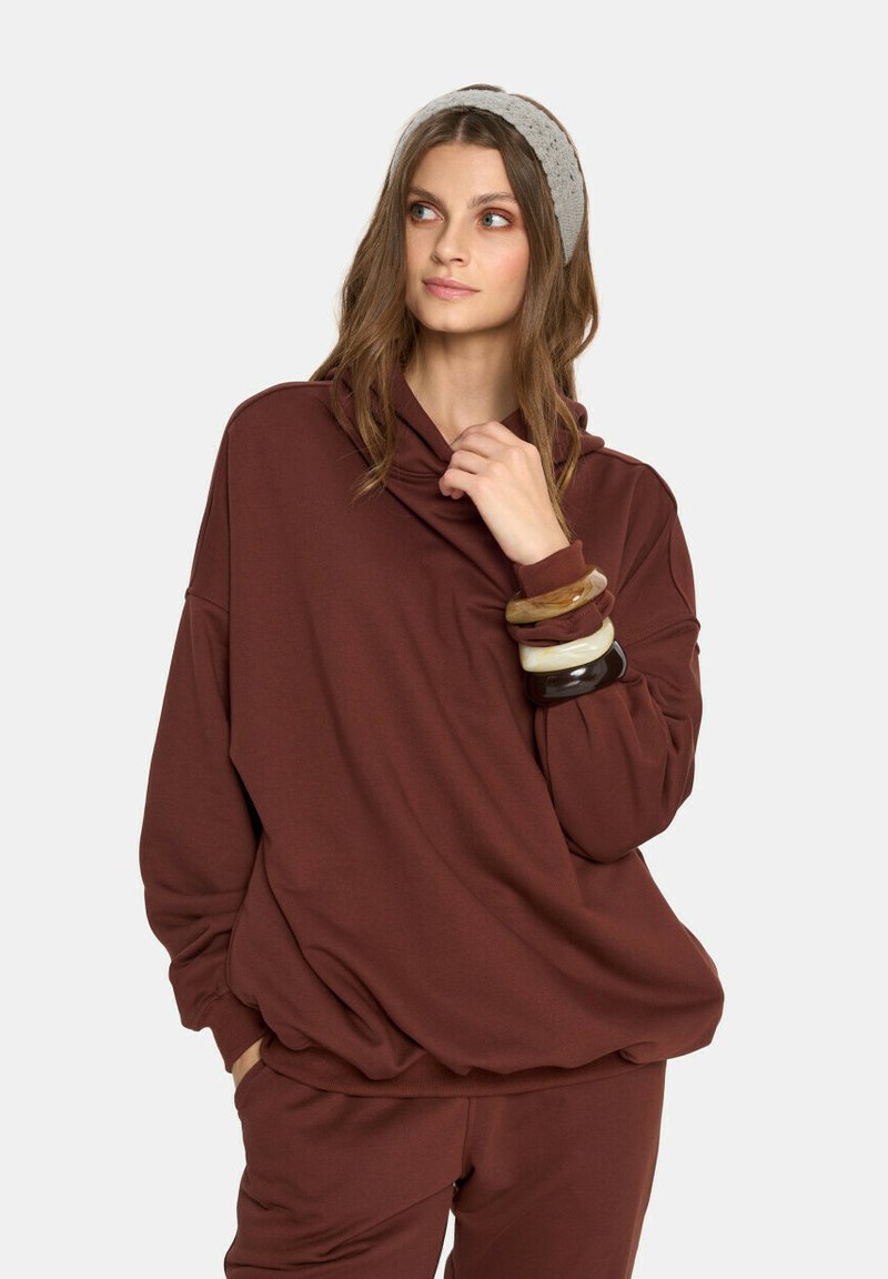 Burgundowy, oversize'owy sweatshirt z kominem, o miękkiej teksturze, długimi rękawami i luźnym kroju, w połączeniu z szarym, dzianinowym opaską na głowę.