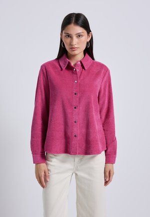 Pink corduroy shirt with a button-down front, long sleeves, and black buttons. Features a structured collar and ribbed texture.