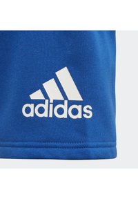 Blue cotton athletic shirt featuring a large white Adidas logo with three stripes. Simple design, short sleeves, and smooth texture.