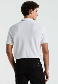 Witte polo met korte mouwen van een gestructureerde stof, voorzien van kleurrijke gestreepte accenten op de kraag en mouwen, gecombineerd met zwarte broek.