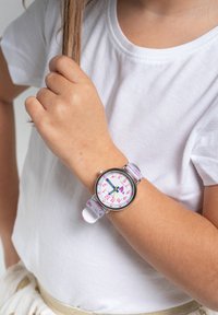 Montre pour enfants avec un bracelet rose et blanc, un boîtier en métal argenté et un cadran blanc avec des marqueurs d'heure colorés et des aiguilles.