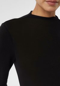Maglietta nera a maniche lunghe con scollo rotondo e texture morbida e liscia. La vista ravvicinata mostra la finitura uniforme del tessuto e una leggera lucentezza.