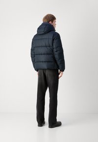 Doudoune bleu marine avec capuche, dotée de sections quiltées horizontales et d'une coupe décontractée, associée à un pantalon en denim foncé et des bottes noires.