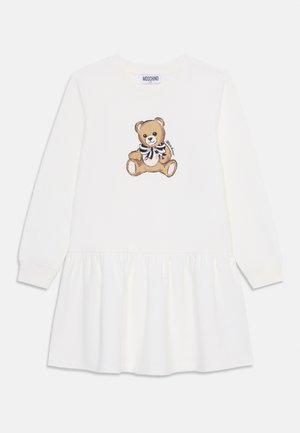 Valkoinen pitkähihainen mekko, jossa on kerrostettu hame. Olkapäällä teddykarhupiirros ruskeissa sävyissä ja musta-valkoisissa yksityiskohdissa.