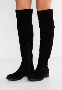 Stivali alti in suede nero con suola piatta, dettaglio con zip sul lato e risvolto nella parte superiore per una vestibilità morbida.