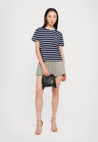 Marineblauw en witte gestreepte t-shirt, korte mouwen, gecombineerd met een grijze plissé rok en een kleine zwarte franjerugzak. Minimalistisch ontwerp, casual stijl.