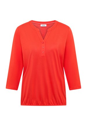 Chemise rouge vif pour femme à manches longues avec trois boutons au col en V et ourlet élastique, portant l'étiquette "CECIL" à l'intérieur du col.