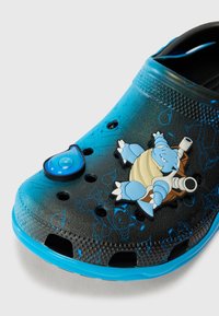 Czarno-niebieskie klapki Crocs z uroczą zawieszką w kształcie kropli wody oraz niebieskim wzorem z rysunkową żółwia. Posiadają perforacje i teksturowaną górną powierzchnię.