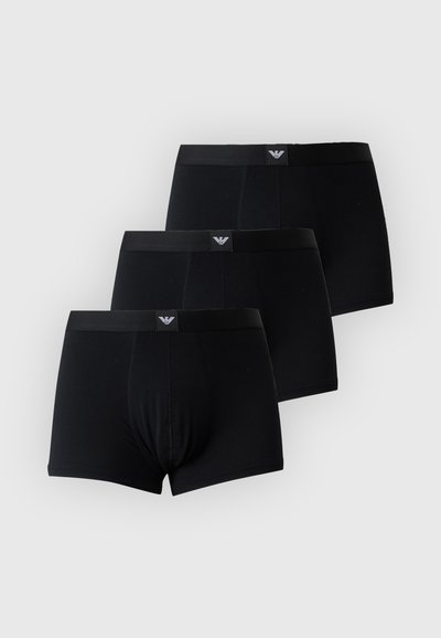 Τρία μαύρα ανδρικά boxer briefs με επώνυμα λάστιχα στην μέση, στοιβαγμένα με ελαφρά μετατόπιση πάνω σε απλό ανοιχτό φόντο.
