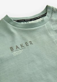Světle zelené bavlněné tričko s kulatým výstřihem, zdobené vyraženým logem "BAKER" a tečkovaným vzorem na jedné straně.