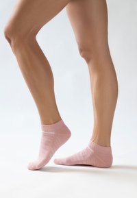 Απαλές ροζ κάλτσες μέχρι τον αστράγαλο με ριμπ τις άκρες, διακοσμημένες με οριζόντιες ρίγες και ευχάριστη υφή, φορεμένες σε γυμνά πόδια που φαίνονται από το πλάι.