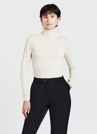Cremfarbener Rollkragenpullover in taillierter Form mit langen Ärmeln, kombiniert mit maßgeschneiderten schwarzen Hosen, die über einen Knopf und ein elegantes Design verfügen.