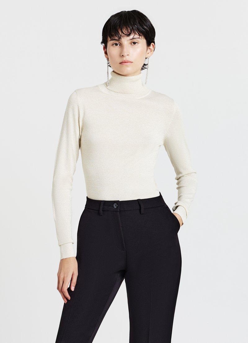 Cremfarbener Rollkragenpullover in taillierter Form mit langen Ärmeln, kombiniert mit maßgeschneiderten schwarzen Hosen, die über einen Knopf und ein elegantes Design verfügen.