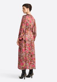 Una modella sta in posizione laterale, mostrando un vestito a stampa floreale con maniche lunghe. Stivali neri con tacco alto completano l'outfit.
