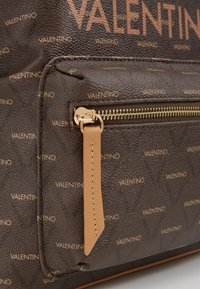 Brun texturerad väska med ett heltryckt Valentino-logomönster, med guldhardware och en dragkedjedetalj i en kontrasterande tanfärg.