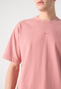 Lyserød bomulds t-shirt med rund hals, korte ærmer og et diskret præget logo på brystet. Blød tekstur med en afslappet pasform.