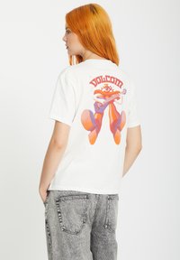 White cotton t-shirt featuring a colorful graphic with a character playing guitar on the back, with "Volcom" text above. Denim pants with faded texture.