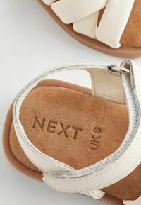 Sandali bianchi in finta pelle con una fascia testurizzata, insole in suede marrone e "NEXT UK 6" impresso sulla suola.