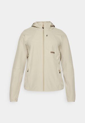 Beige lett jakke med hette, glidelås foran, to sidelommer og en liten logo detalj på brystet. Glatt tekstur på stoffet.