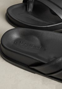 Sandales slides noires avec semelles texturées et « N. PREMIUM COLLECTION » embossé sur la semelle intérieure, placées sur une surface claire.