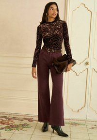 Burgundia laienevad püksid, mis on paari pandud mustrilise sametist pikkade varrukatega blouseega. Aksessuaarid sisaldavad pruuni vööd ja tumedat kotti. Mustad terava ninaga kontsad.