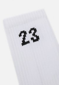 Calcetín blanco con canalé y el número "23" tejido en negro en la zona del tobillo, que presenta una textura suave y material elástico para mayor comodidad.
