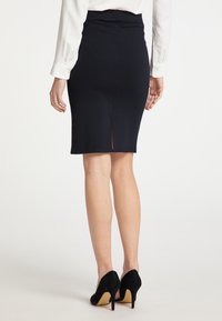 Zwarte fitted rok met een achterkant split, gemaakt van rekbare stof. Gecombineerd met zwarte hoge hakken, die een soepele textuur en een op maat gemaakt ontwerp laten zien.