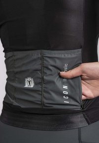 Black athletic top with a gray mesh pocket at the waist, featuring a logo and text. Fabric appears smooth; seam detailing is visible.