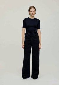 Cămașă scurtă de culoare bleu marin, asortată cu pantaloni negri cu talie înaltă și laturi largi, având o textură netedă și un design minimalist. Accente de încălțăminte neagră.