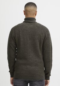 Strickpullover in dunklem Olivgrün mit hohem Kragen, strukturiertem Muster und gerippten Bündchen und Saum.