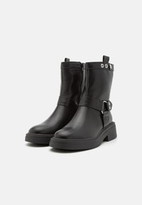 Botas de cuero negro hasta el tobillo con una cremallera lateral, una correa ancha con acentos metálicos y un tacón grueso. Textura suave y diseño minimalista.