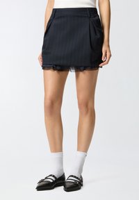 Tamna mornarsko plava mini suknja s nabranim detaljima, prugama, prozirnom volan-hemom i bočnim džepovima. Uparena s crnim cipelama i bijelim čarapama s prugama.