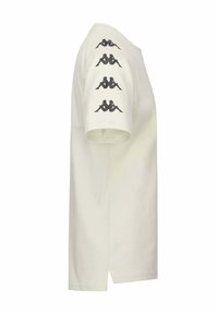 T-shirt à manches courtes de couleur crème en coton. Présente des imprimés graphiques noirs sur les épaules dans un motif répétitif. Ourlet droit.