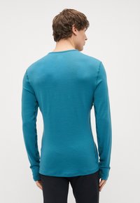 Camisa de manga longa em teal, feita de tecido suave, com um decote arredondado, corte slim e detalhes de costura mínimos nas laterais.