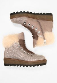 Botas de invierno de ante beige con borde de piel, suelas gruesas de goma marrón estriadas, ojales de metal, cremalleras laterales y adornos de strass y perlas en la parte frontal.