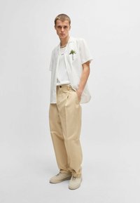 Short-sleeve white shirt with palm tree design, layered over a white tank top, paired with beige wide-leg pants and light beige sneakers.