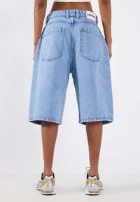 Light blue denim shorts with a relaxed fit, featuring a black branded waistband and two back pockets. The fabric has a soft texture.