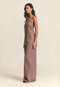 Světle hnědý top bez ramínek v kombinaci s širokými kalhotami ze stejného materiálu. Hladká textura a jednoduchý design nabízejí uvolněnou siluetu.