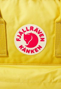 Gul ryggsäck med texturerat tyg som har en rund logotyp och röd text. Inkluderar vadderade remmar och ett dragkedjefack.