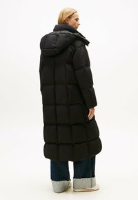 Zwarte pufferjack met gequilt ontwerp, lange lengte en grote capuchon. Gecombineerd met wijde jeans met rafelrand en lichtgekleurde sneakers.
