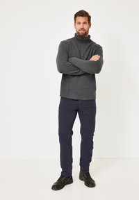 Dunkelgrauer Rollkragenpullover aus strukturiertem Strick, kombiniert mit marineblauen Hosen und schwarzen Schnürschuhen. Minimalistisches Design, gerade Passform.