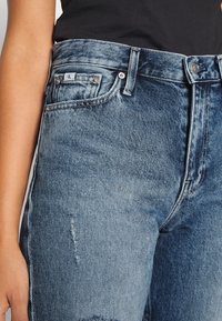 Jeans i blekt blå denim med lätt slitage, som har en traditionell femficksdesign och metallknappstängning.